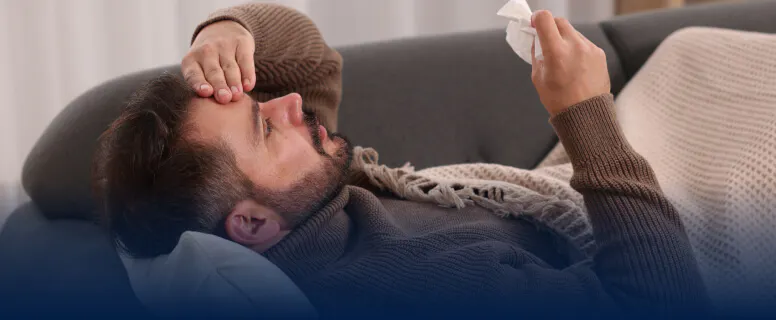 Homme couché sur un canapé et se tenant la tête, en proie à une douleur