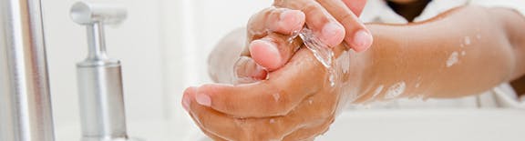 Close-up of a child’s little hands being washed with soap and water over a white sink