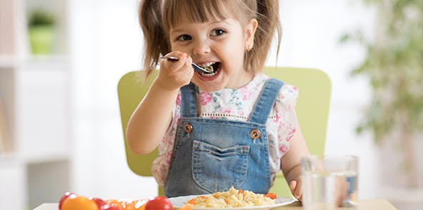 Toddler girl eating vegetables in a high chair