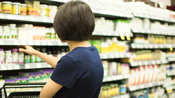 A woman selecting a bottle of vitamins from a store’s shelf.