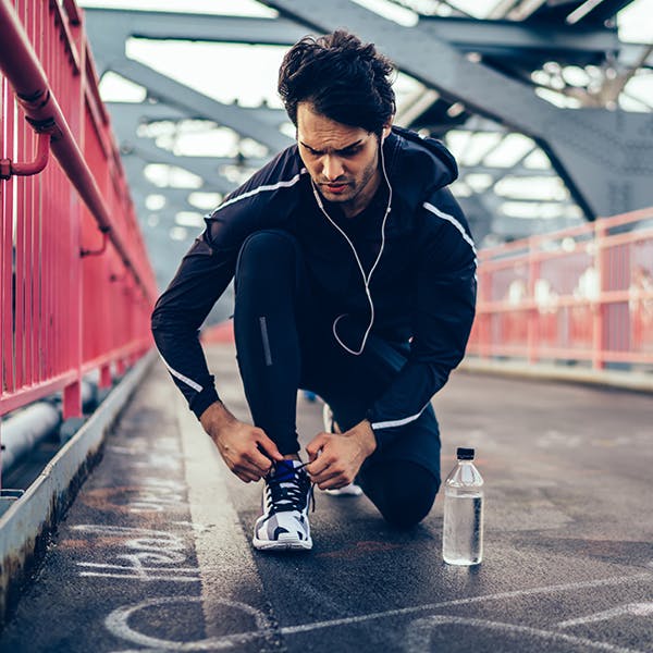 Man kneeling to tie his shoes while outside on a run