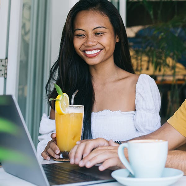 Smiling woman holding a drink looking at a laptop