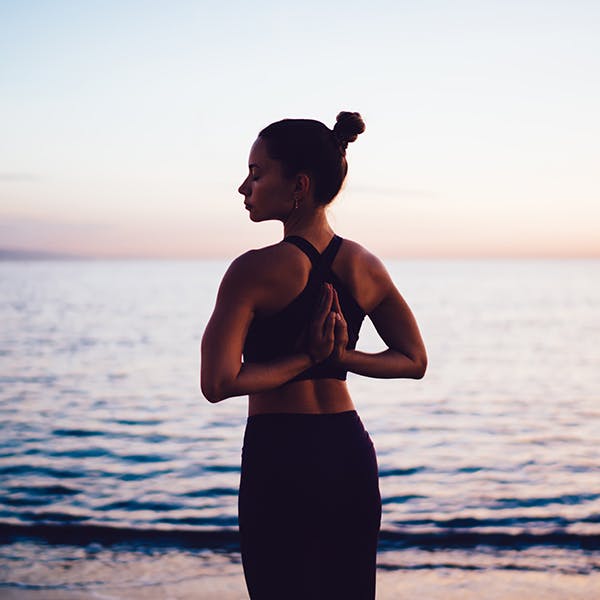 Woman stretching with her hands behind her back at the beach