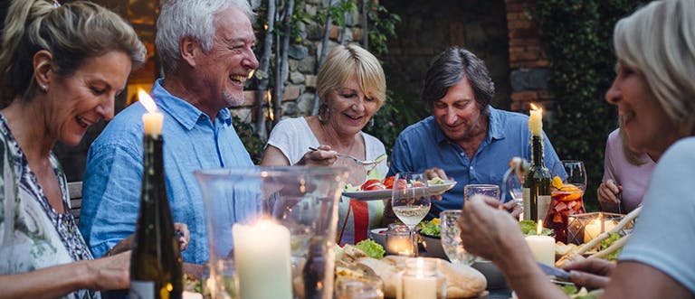 Skupina starších lidí sedící u stolu u společného jídla.