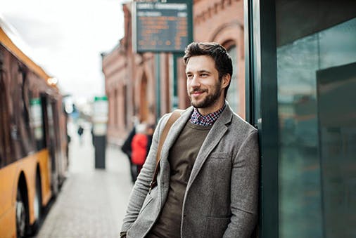 Mann mit Bart steht nonchalant an einer Bushaltestelle