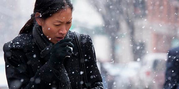 Coughing woman walking through falling snow.