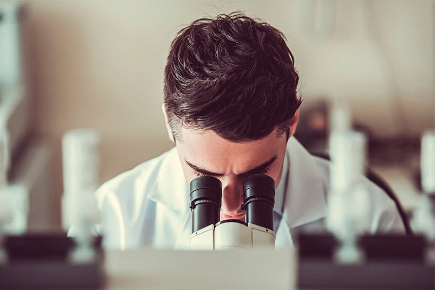 Man in a lab coat looking into a microscope