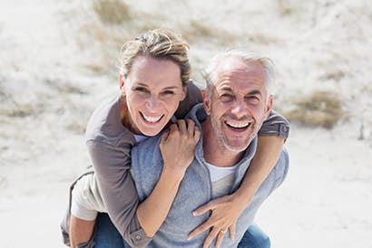 Elderly man giving a woman a piggyback ride on the beach.