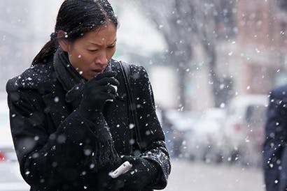 Coughing woman walking through falling snow.