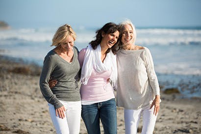 Három idősebb hölgy sétál a strandon.