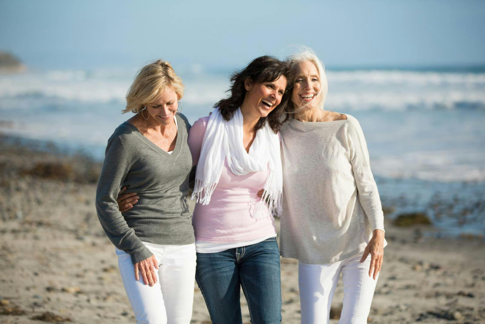 Drie oudere dames die over het strand lopen.