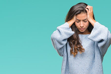 A visibly stressed woman in a blue sweater holding her head