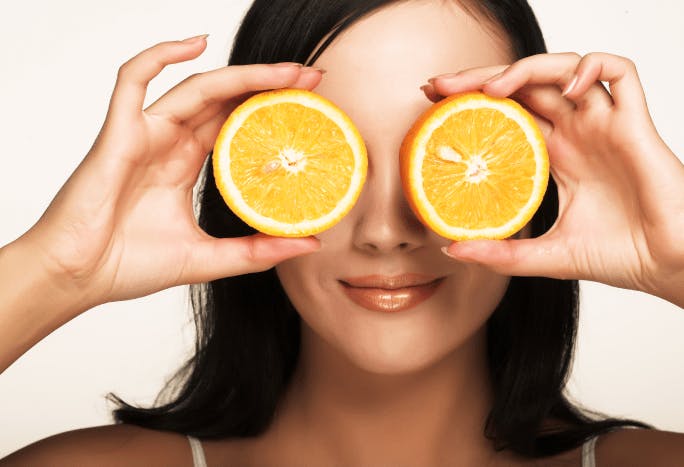 Woman holding two orange slices against her eyes.