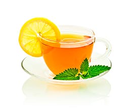 Chai a L'orange tea drink in a clear teacup with a lemon wedge and mint sprig