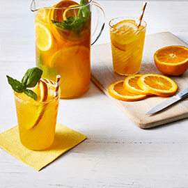 Pitcher and glasses filled with Orange Basil Sparkler drink beside slices of fresh orange