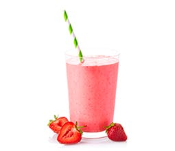 Strawberry Smoothie Surprise in glass with green and white stripes and fresh strawberries around base of glass 