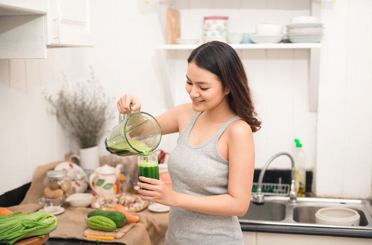 Woman pouring green smoothie into a glass