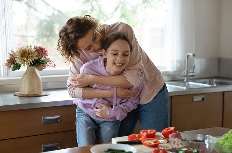 Mother hugs pre-teen daughter in kitchen