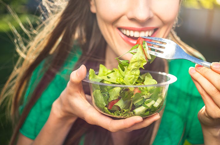Portrait of woman smiling and eating green salad