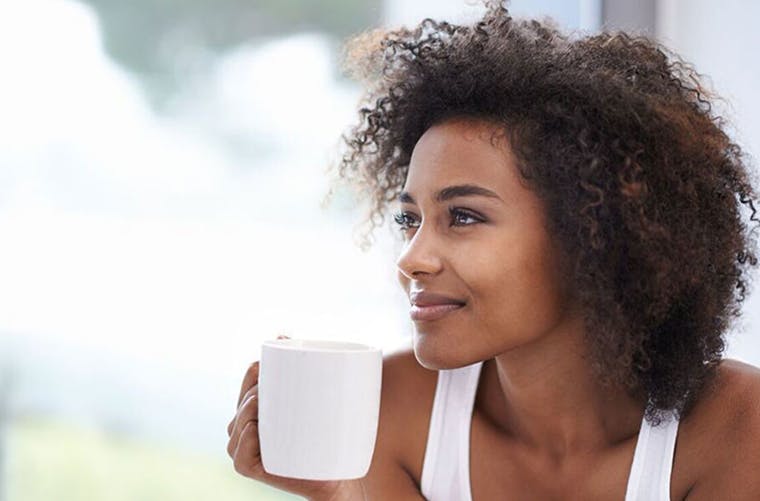 Young black woman with natural hair smiles while drinking a cup of coffee