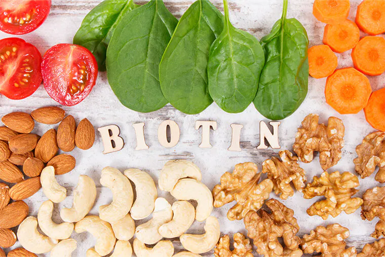 Food containing biotin (B7) – including tomatoes, spinach, carrots, walnuts, cashews, and almonds – on a white background.
