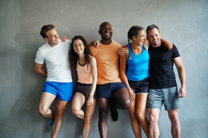 Smiling group of friends in sportswear laughing together while standing arm in arm in a gym after a workout.