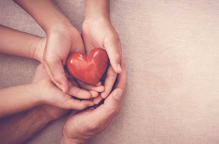 Adult hands cupping child’s hands holding a heart-shaped red stone