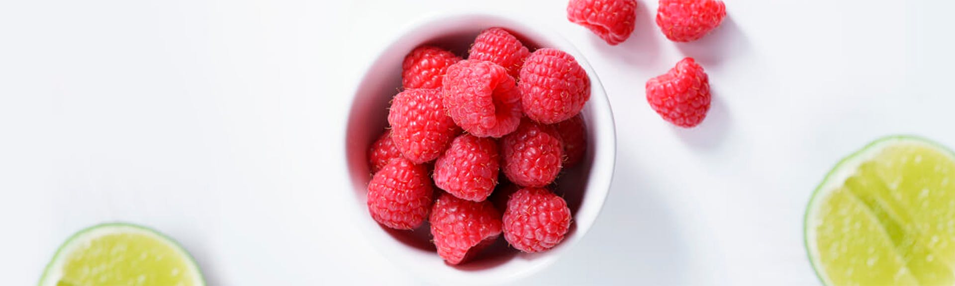 Cup of fresh red raspberries aside slices of lime