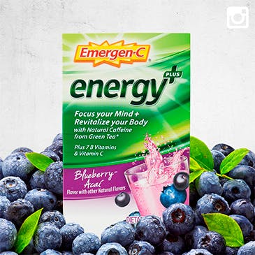 Package of Emergen-C Energy Plus in Blueberry-Acai flavor resting on a pile of fresh blueberries.