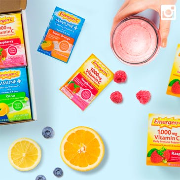 Packets of Emergen-C in different flavors resting beside fresh fruits and a glass of Emergen-C. 