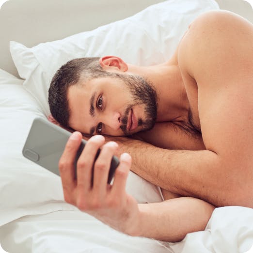 Man lying in bed, looking at his phone with a serious expression