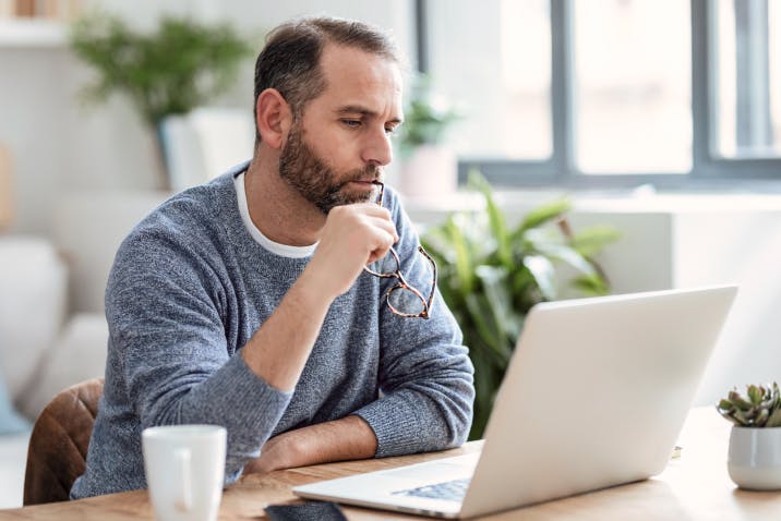 Man pondering while working on a laptop in a well-lit living room