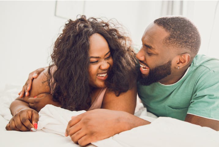 Joyful couple on a bed, woman laughing as man whispers in her ear