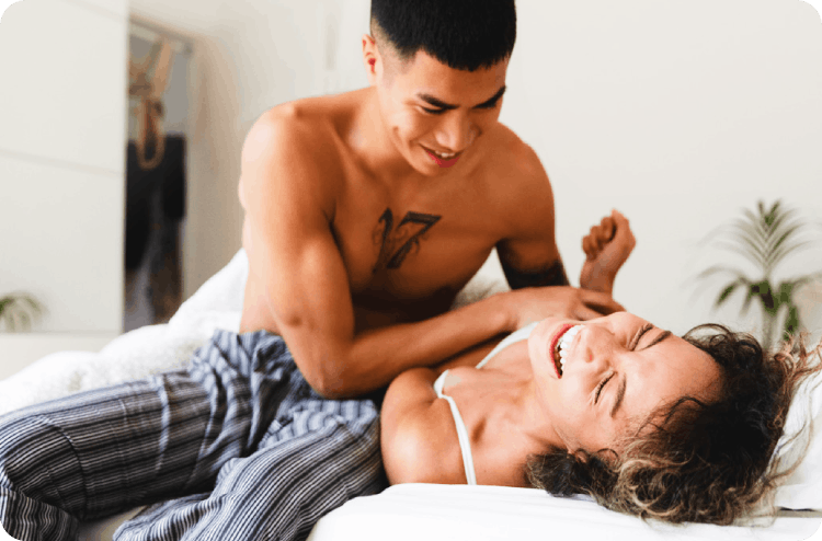 Man and woman playful on a bed, both smiling broadly