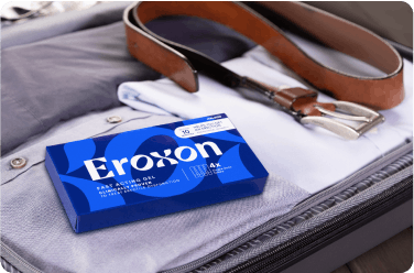 An open suitcase with clothes, a smartphone, and a box of Eroxon inside.