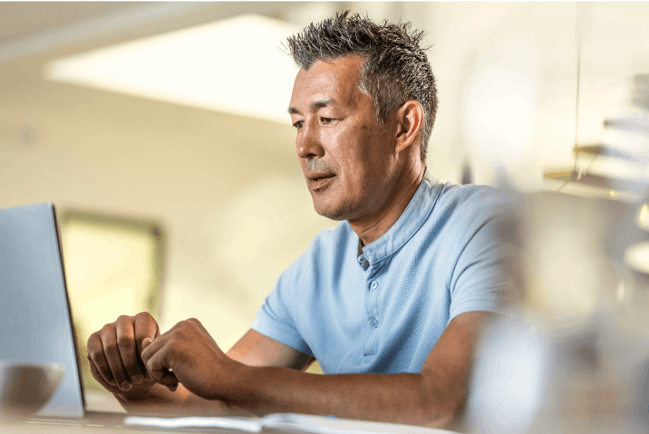 A man sitting at a desk, focused on his laptop screen, appearing engaged in his work.