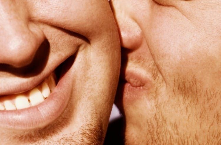 A close-up of two people smiling, one person whispering to the other.