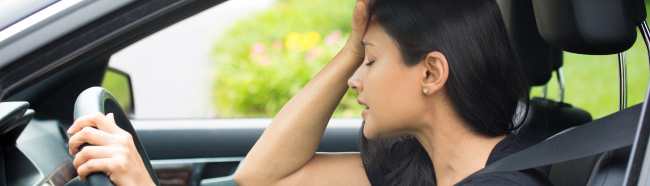 woman holding head while driving a vehicle