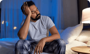 Man with nighttime headache sits on bed holding his head