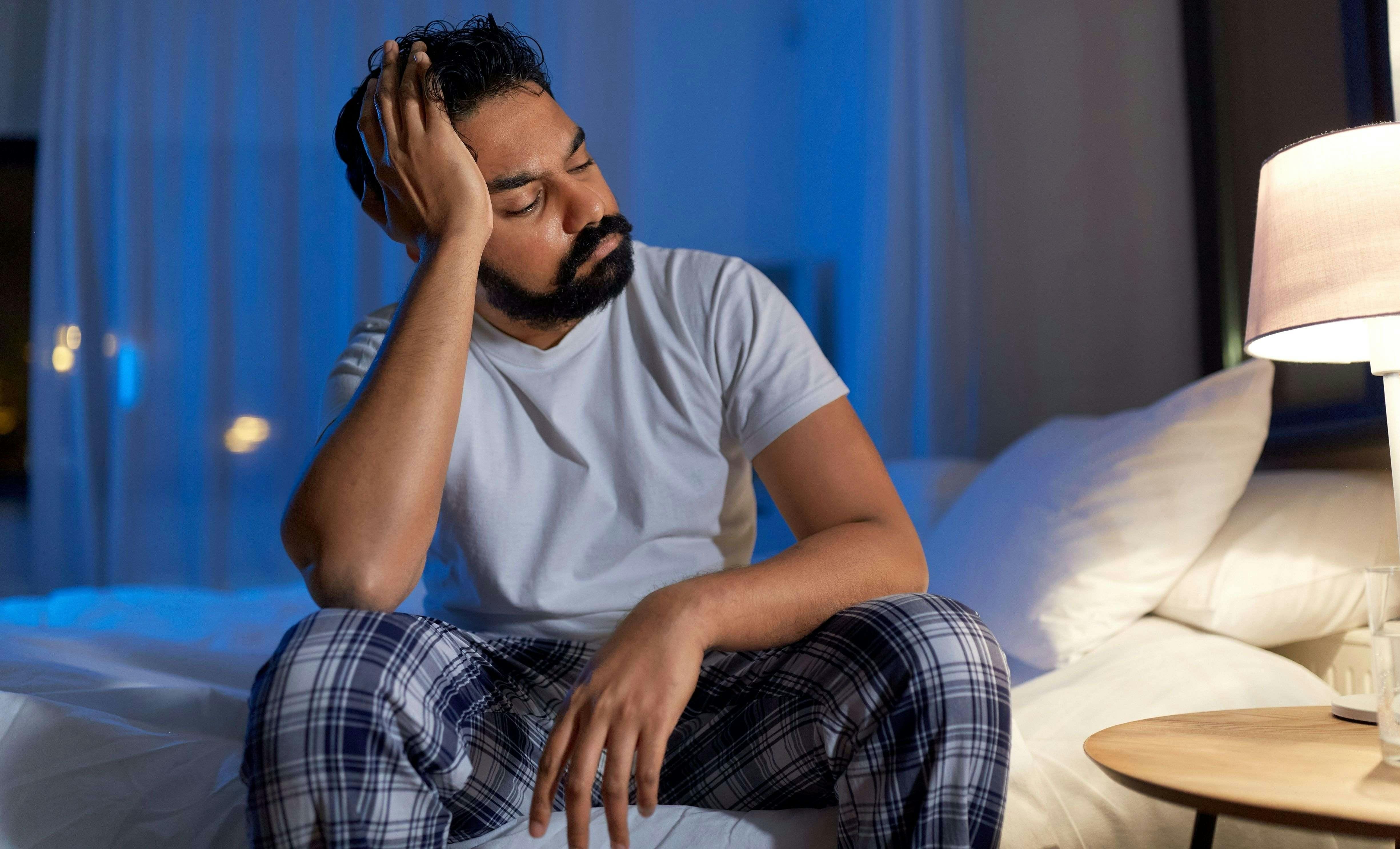 Man with nighttime headache sits on bed holding his head