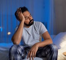 Man with nighttime headache sits on bed holding his head