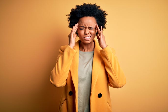 Woman wearing a yellow jacket suffering with a migraine