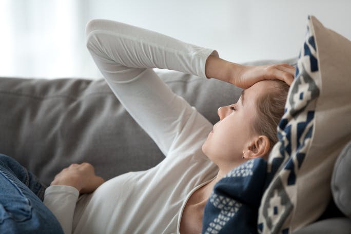 Young woman on couch suffering from migraine and fever