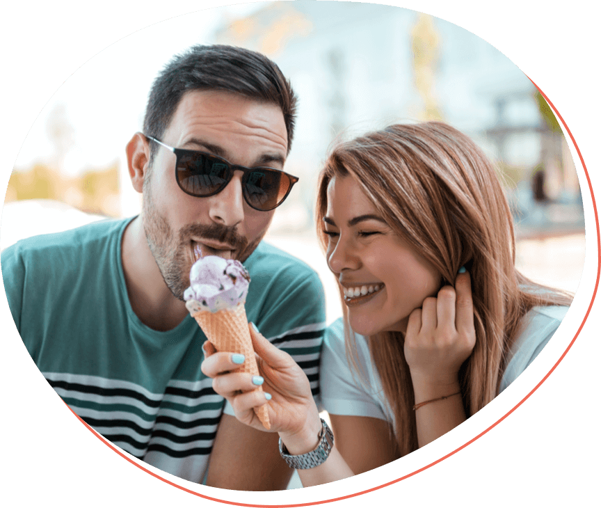 a young couple, the man wearing sunglasses and a dirty blonde woman, enjoying blackberry ice cream while smiling