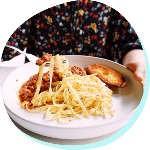 person lifting up pasta on a fork from a plate full of pasta, sauce, and bread
