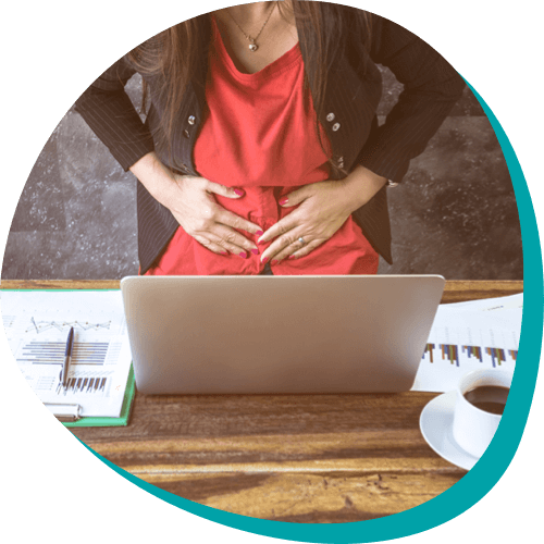 woman wearing a red dress holding stomach in discomfort while looking at laptop