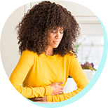 image of a woman with very curly hair holding stomach in discomfort while wearing yellow shirt
