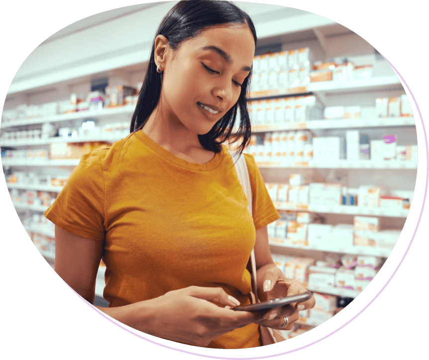 young dark-haired woman with mustard yellow t-shirt looking at phone while in a pharmacy