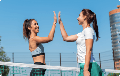 Two young woman in workout clothes giving high-fives over a tennis net