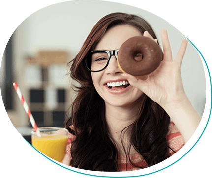 young brunette woman with black plastic glasses holding a chocolate donut and a glass of orange juice
